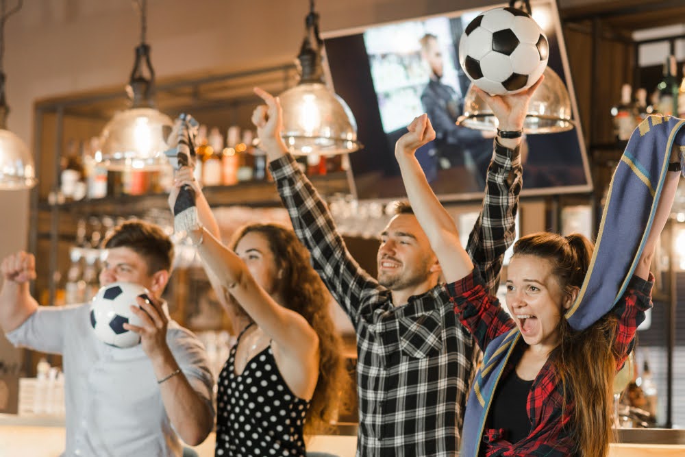 People excitedly cheering while watching a soccer game in a bar.
