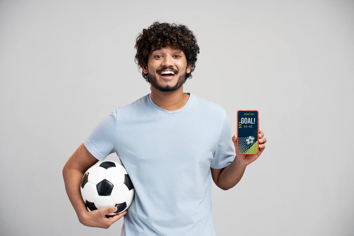Man holding a ball and a mobile phone with open betting software. 
