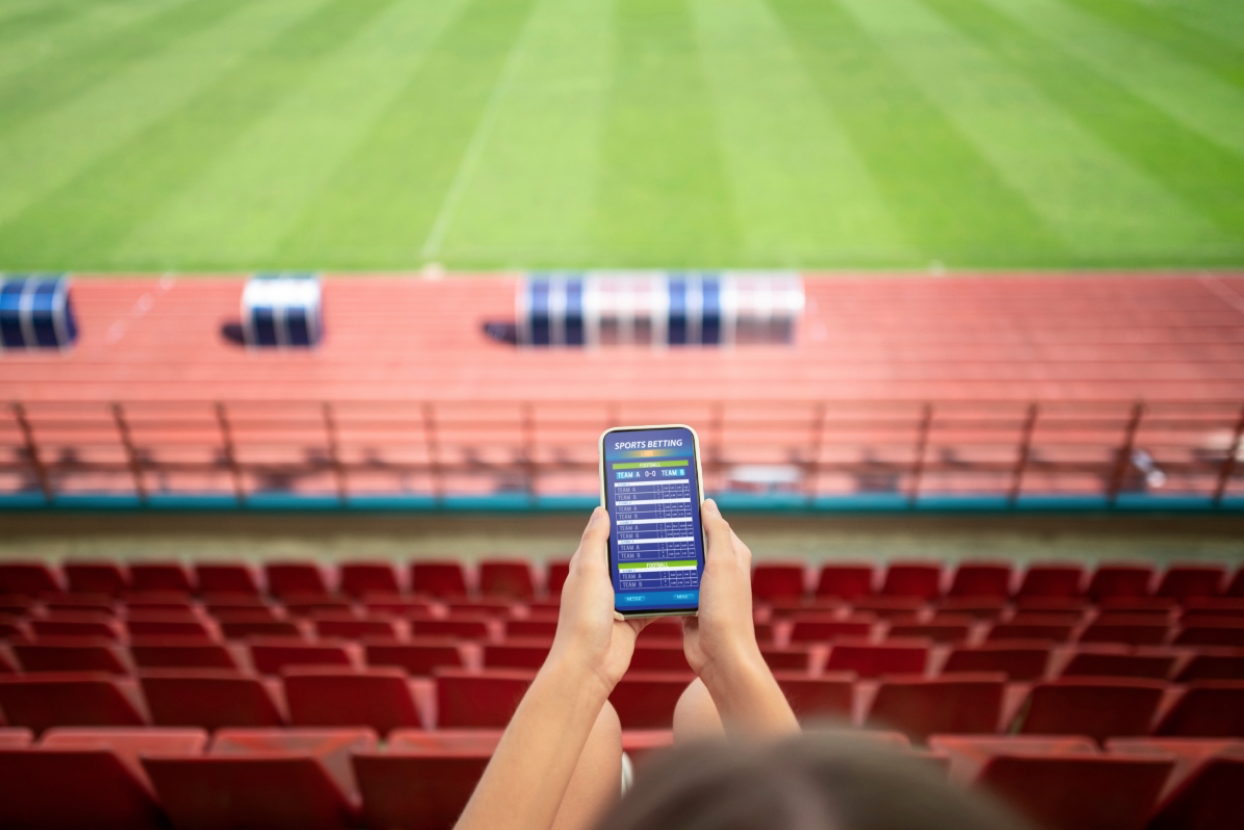 Bettor placing live football bets on a smartphone at the stadium. 