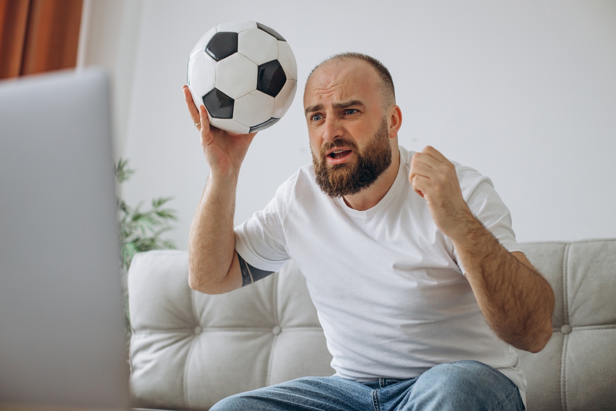 A man holding a football and watching soccer.